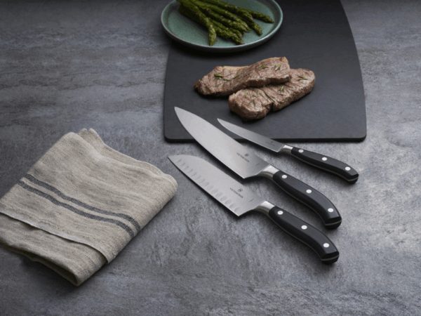grant maitre kochmesser schwarzer griff auf dunklen untergrund mit schneidbrett, auf dem ein felitiertes fleisch und spargel liegt