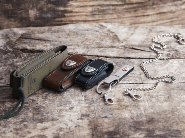 auswahl verschiedener leder gürteletuis grün, braun, schwarz messerkette und multiclip in silber auf holzboden